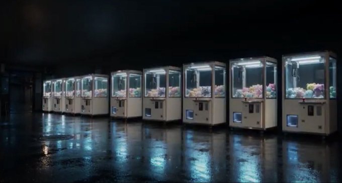 A row of illuminated claw machines lined up in a dark, wet-floored arcade.
