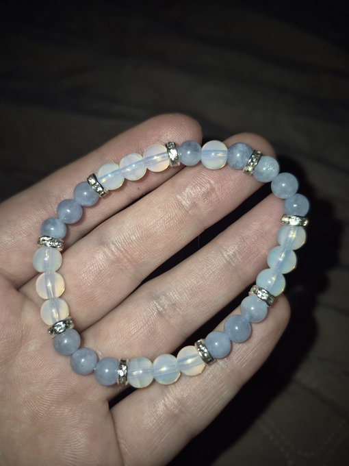A hand holding a beaded bracelet made of round light blue, white, and pale opalite-like stones separated by silver rhinestone spacer beads.