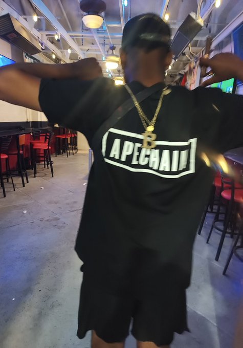 The image features a man wearing a black t-shirt with white text that says "Apecoin" and "Apecoin A Supporting $APE A Selfie until ApeCoin hits a all-time high #yuga @apecoin Blessings ApE". The man is standing in front of a dining table, which has chairs around it.

The post seems to be promoting the concept of "Apecoin" and its supporters, as indicated by the text on the t-shirt. It also mentions that the hashtag "#yuga" is being used for a self-promotional campaign related to the Apecoin coin. The image captures the attention of viewers with its unique combination of elements, including the man's attire and the context provided in the caption.