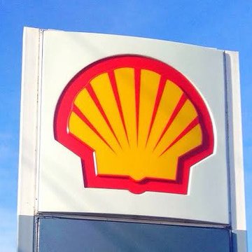 The Shell logo, featuring its iconic yellow and red scallop shell emblem on a white sign against a blue sky, is displayed prominently to visually represent the oil giant mentioned in the post about Shell accepting Bitcoin payments via the Lightning Network in Africa.