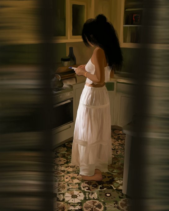 A woman with long dark hair, wearing a white tube top and long flowing skirt, stands barefoot in a kitchen looking at her phone.