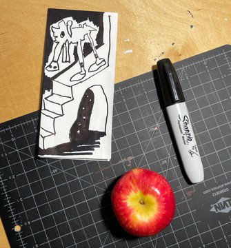 A sketch on a canvas depicting the AT-AT walker from Star Wars descending stairs, photographed on a black cutting mat alongside a Sharpie marker and a red apple.