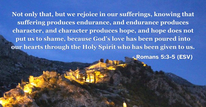 A Bible verse from Romans 5:3-5 (ESV) is displayed over a nighttime photograph of an illuminated hillside village.