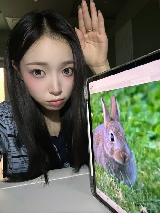 A split selfie showing the same young woman on the left with a serious expression and her hand raised behind her head, juxtaposed on the right with an image of a brown rabbit on green grass.