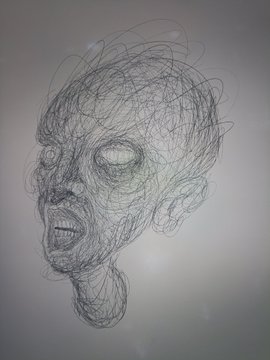 A wireframe sculpture of a screaming or distressed face made of tangled wire, viewed from the side.