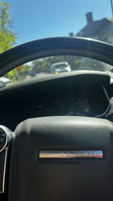 View from inside a Range Rover, showing the steering wheel with the "RANGE ROVER" emblem and a street scene through the windshield.