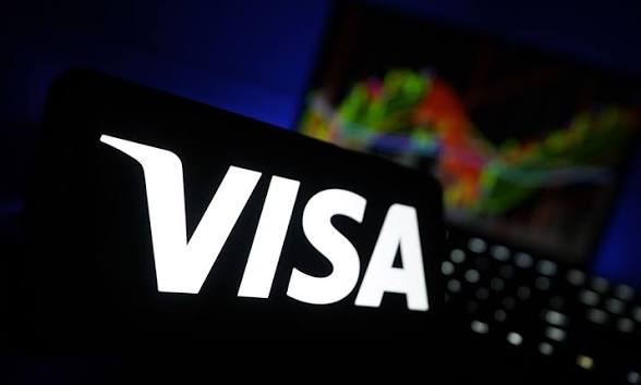 The illuminated VISA logo displayed on a screen with a laptop in the blurred background.