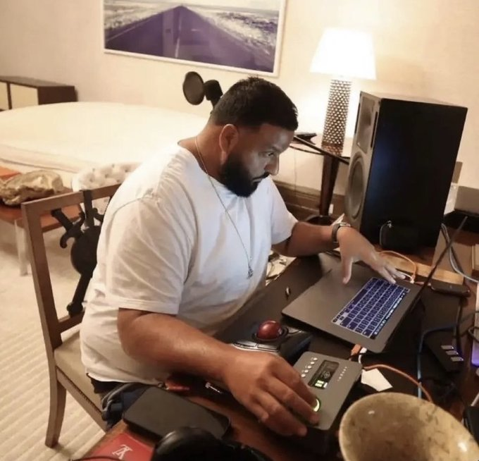 A bearded man in a white t-shirt sits at a desk late at night, focused intently on his laptop while operating audio equipment, appearing to be in deep concentration—fitting the post's self-deprecating humor about the obsessive, sleepless pattern of chasing losing crypto investments.