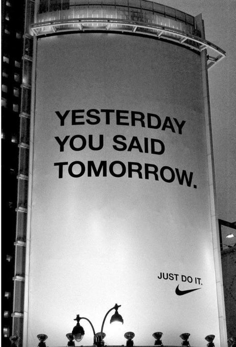 A large billboard displays the text 'YESTERDAY YOU SAID TOMORROW. JUST DO IT.' alongside the Nike swoosh logo, captured in black and white.