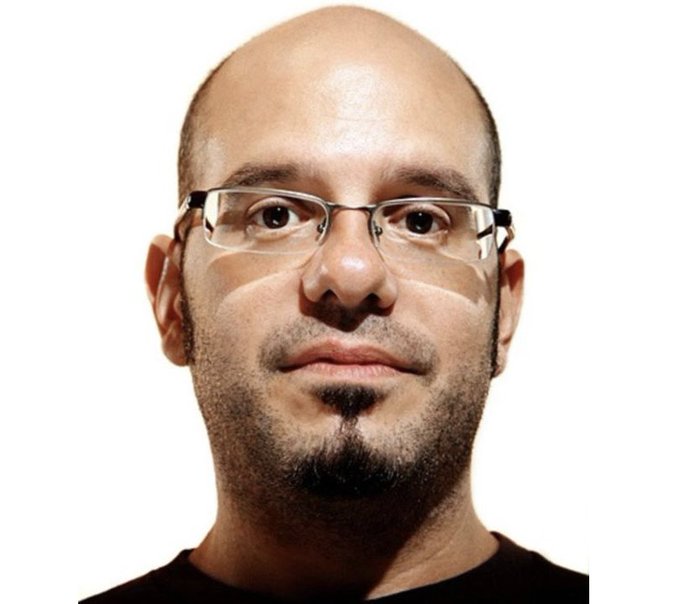 A headshot photograph of a bald man with glasses, a goatee, and a soul patch against a white background.