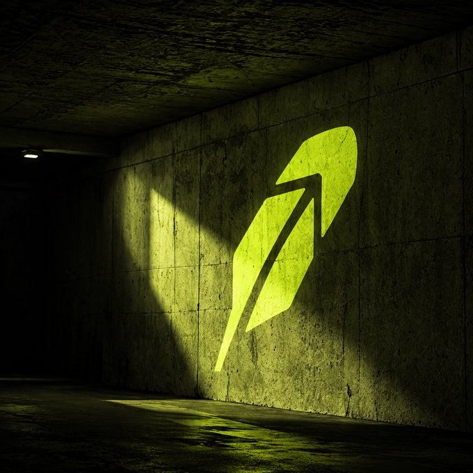 A glowing green feather logo, the iconic symbol of Robinhood, is projected onto a dark concrete wall, illuminated dramatically by a beam of light. The minimalist image reflects the post's sentiment, symbolizing how the platform's streamlined trading experience can be a transformative, shining presence in someone's financial journey.