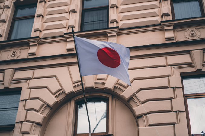 A Japanese flag flies outside an ornate building, symbolizing the partnership between SBI Holdings and Ondo Finance to tokenize Japanese equities and expand the use of the JPYSC stablecoin for settlement and collateral.