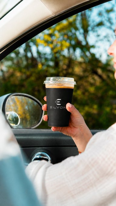 A person sits in a car holding a black coffee cup branded with the "ELYON" logo, symbolizing a fresh start to the day. The image reinforces the motivational message about new opportunities and building momentum within the Elyon community, with the airdrop link inviting participation.