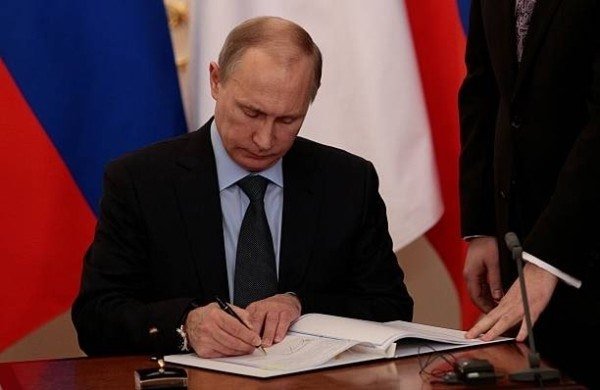 Russian President Vladimir Putin is shown signing documents, an image illustrating news reports that he has signed a bill to regulate and incorporate the cryptocurrency market into Russia's formal financial system.