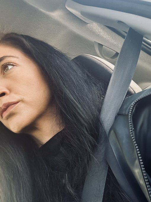 A woman with long black hair sits in a car, gazing out the window thoughtfully while wearing her seatbelt, visually reinforcing her post's theme of taking action and making life changes when XRP isn't moving.