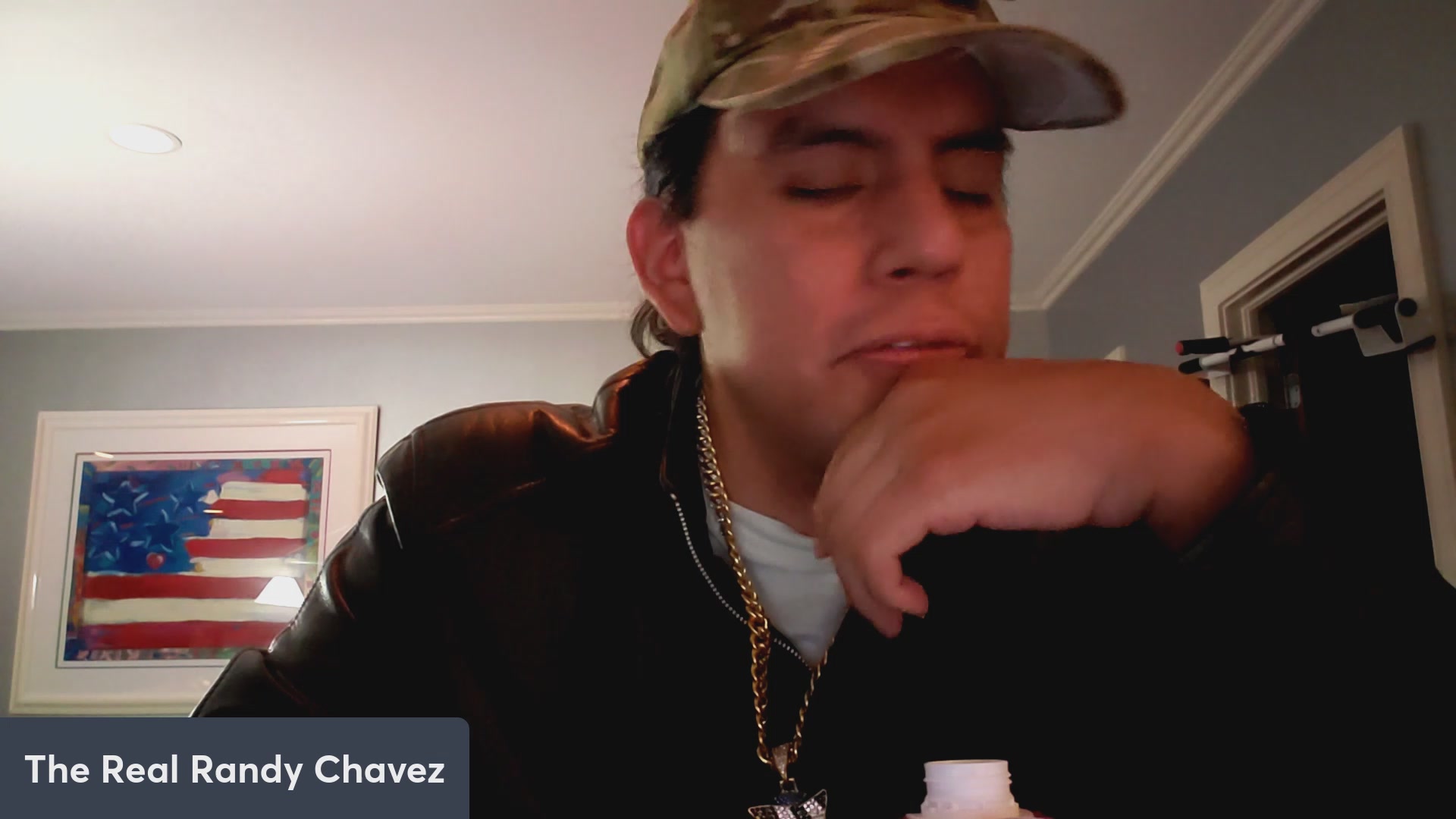 The image features a man wearing a camo hat, sitting at a table with his hand resting on his chin. The background of the image includes an American flag, suggesting that this could be taking place in a country where the flag is prominently displayed. The caption reads "VeVe continues it' s user rally! $OMI Dacat speculation!" and "AMA!", which are likely part of a discussion or conversation about the content on the post.