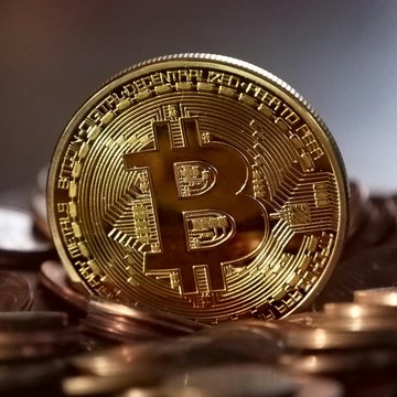 A gold-colored Bitcoin coin is prominently displayed in the foreground, resting on a pile of copper coins. The image visually represents the cryptocurrency rally discussed in the post, highlighting Bitcoin's current market activity amid tactical futures positioning and surging hot capital.