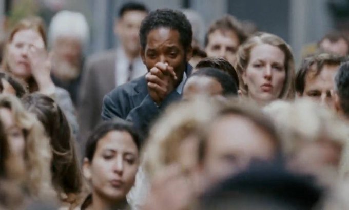 The image shows a man wearing a suit, surrounded by a crowd of people who are also dressed up for an event or gathering. They appear to be engaged in conversation with each other. The scene takes place outdoors, possibly at a social function or a public space where people have gathered together.