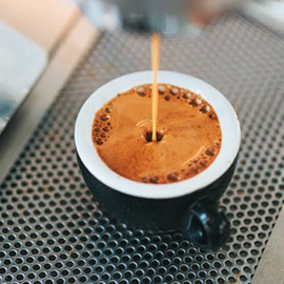 A close-up shot of espresso being pulled into a small black cup on a perforated metal drip tray of an espresso machine.