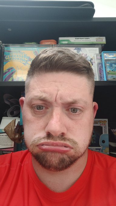 A man in a red shirt making a sad, pouty face, with Pokémon trading card game products visible on shelves behind him.