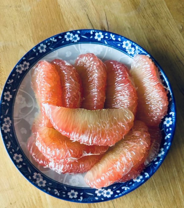 A blue-and-white floral ceramic bowl filled with peeled pink grapefruit segments sitting on a wooden table.