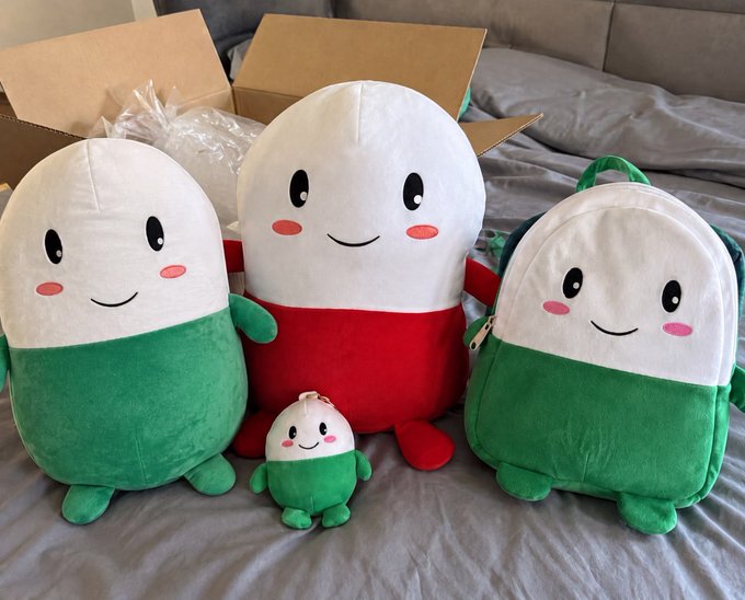 A collection of plush toys and a matching backpack from the Pump.fun "Cupsey" mascot merchandise line, displayed together on a bed. The caption highlights the user's enthusiasm for owning the full Cupsey product lineup and teasing that the Pump.fun mascot won't fade in popularity, predicting it will reach a $100 million market cap.