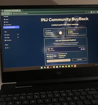 A laptop screen showing the INJ Community BuyBack interface with information about limited spots left and a YouTube link.