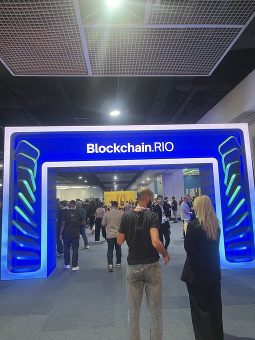 Photo of the entrance to the Blockchain.RIO event, featuring a blue illuminated archway with people gathered around the entry.