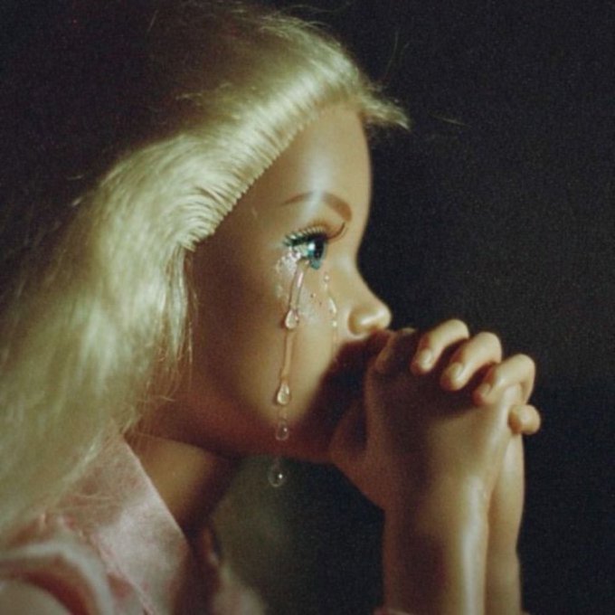 Vintage photograph of a blonde woman in profile with clasped hands, featuring artistic tear droplets running from her eye.