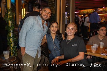 Three people pose together at an event, with logos at the bottom for 'MOMENTUM CAPITAL SOLUTIONS,' 'mercuryo,' 'turnkey,' and 'Flex.'