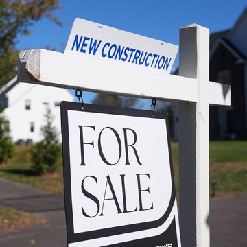 A "NEW CONSTRUCTION" and "FOR SALE" sign is displayed in front of a house, reflecting the housing market context in which rising US mortgage rates—now around 7.6% on 30-year fixed loans—are making new home purchases more expensive for buyers.