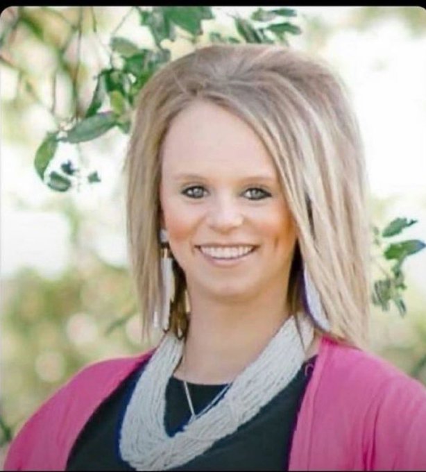 A young woman with blonde hair and a pink cardigan smiles outdoors in a professional portrait photograph.