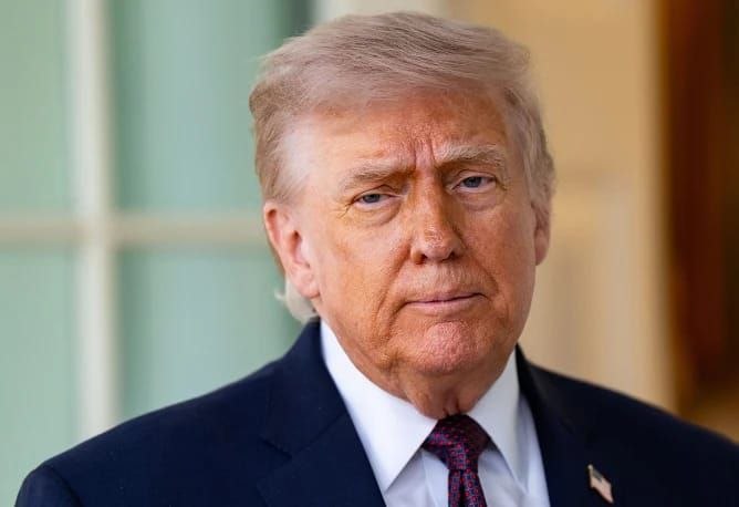 The image depicts a photo of the former U.S. President Donald Trump posing for the camera. He has a serious expression on his face as he looks at the photographer with an unwavering gaze. The photograph captures the essence of the moment, giving viewers insight into the historical and political context surrounding the event.