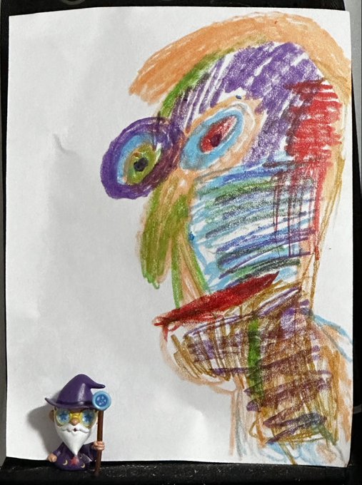 A child's colorful crayon drawing of a face with prominent eyes and hair is pinned up, with a small wizard cat figurine sitting in the bottom left corner.