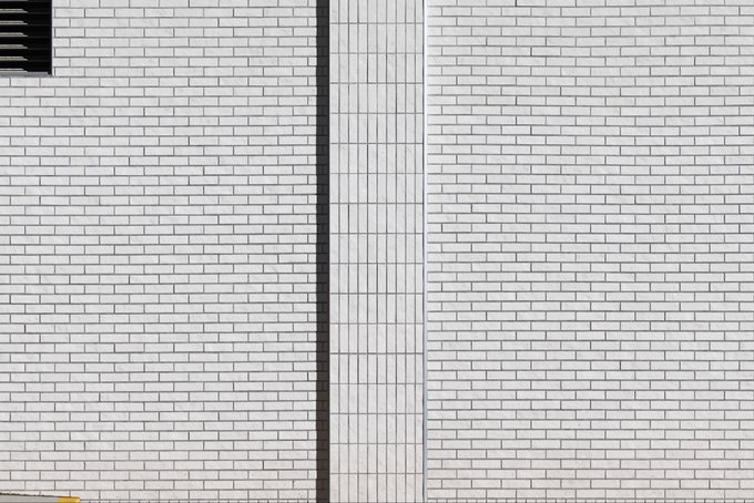 A photorealistic rendering of a white brick wall with vertical metal slats, characteristic of Tyler Hobbs' algorithmic art piece "The Wall." The image showcases the subtle variations in brick texture and shading that result from hand-coded algorithms attempting to mimic real-world surfaces.