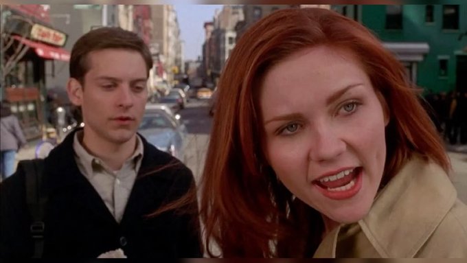 The image shows Tobey Maguire and Kirsten Dunst in a scene from Spider-Man on a city street, with Dunst speaking into the camera and Maguire appearing subdued behind her. The caption humorously suggests Maguire looks "broke" because, as the post implies, he has invested all his money in $ANSEM.