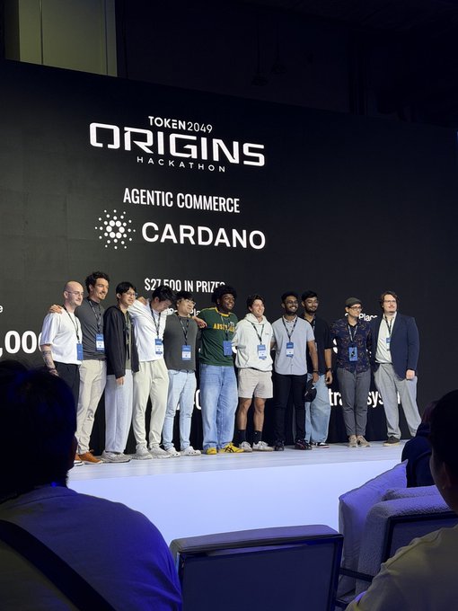A group of hackathon participants pose on stage at the TOKEN2049 ORIGINS HACKATHON, sponsored by Cardano with $27,500 in prizes for 'Agentic Commerce.'