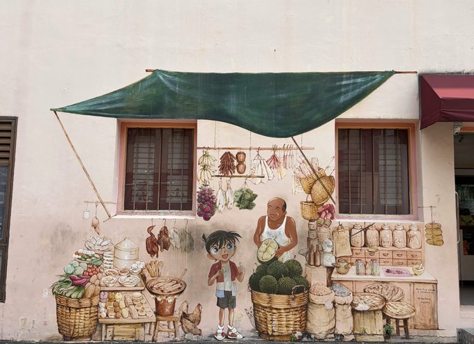 A colorful street mural depicting a traditional market scene with a young boy, a vendor, baskets of produce, and hanging dried goods under a green awning.