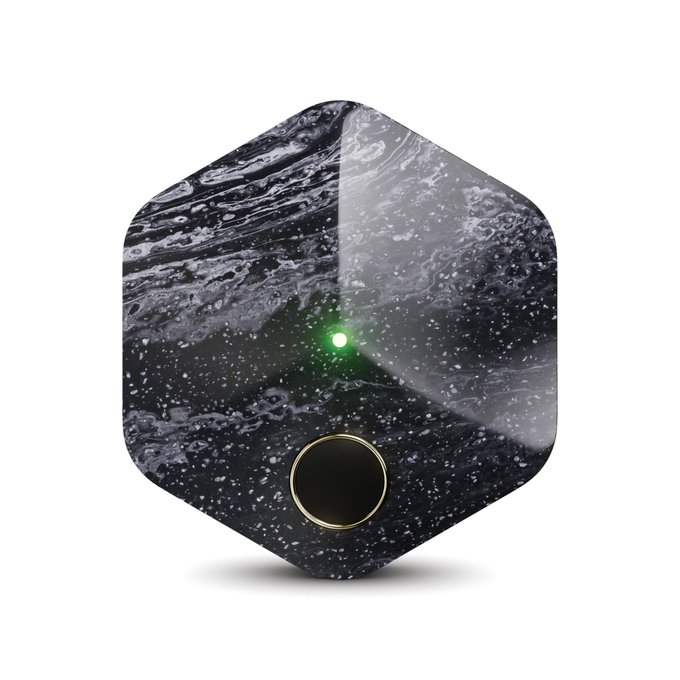 A hexagon-shaped Bitkey hardware wallet featuring a glossy black marbled finish with a glowing green LED indicator and a gold-ringed circular button is displayed against a white background. The image relates to the post by visually showcasing the Bitkey device, helping illustrate the hardware wallet being questioned about its lack of widespread adoption.