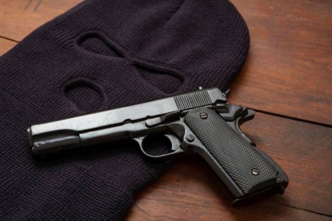 A photograph of a black semi-automatic pistol resting on a dark blue ski mask atop a wooden table.