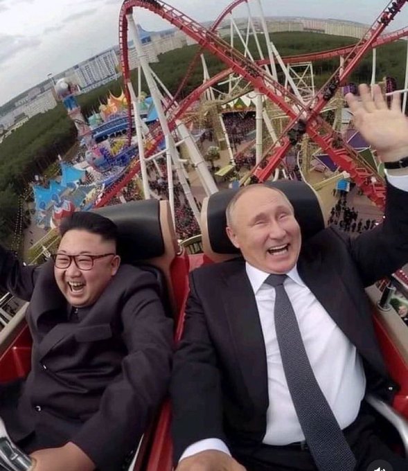 The image shows two men wearing suits, one of whom has a tie visible, riding a roller coaster together. They are both smiling and waving at the camera while enjoying their ride. The caption "When you and your friend both 100X" suggests that they might be friends or acquaintances who have decided to share this experience together as a fun activity.