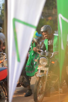 A man in a green vest and helmet sits on a motorcycle in a busy street, framed by green and white promotional banners. The image appears to capture the launch event of Delta Cash, an express car loan service offering funding from 2m to 300m.