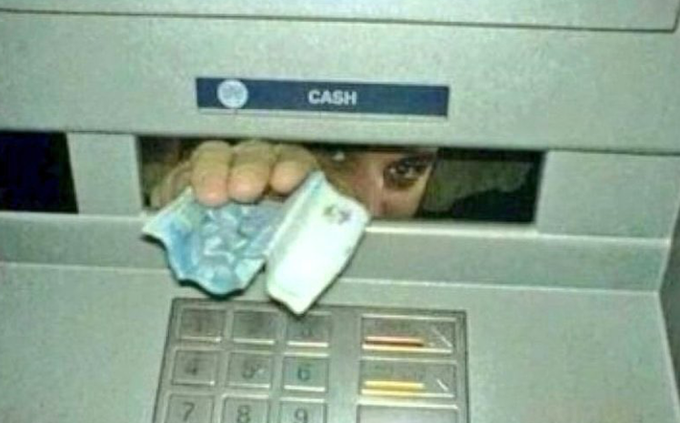 A person partially visible behind an ATM's cash dispenser, holding a stack of banknotes with a glitchy, distorted visual effect.