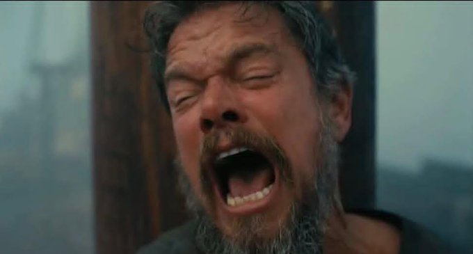 A close-up of an older bearded man screaming with his eyes squeezed shut, appearing to be in extreme pain or anguish.