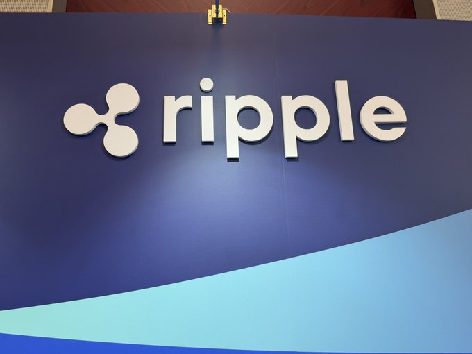 The Ripple logo is displayed on a blue background with a light blue wave design at the bottom.