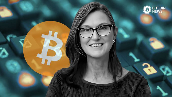 The image features a grayscale portrait of Cathie Wood smiling and wearing a dark sweater and glasses, set against a background of a stylized keyboard with cryptocurrency icons, including a prominent orange Bitcoin logo, with "BITCOIN NEWS" text in the top right corner—visually reinforcing the post's claim about Bitcoin's transformative economic impact when combined with AI.