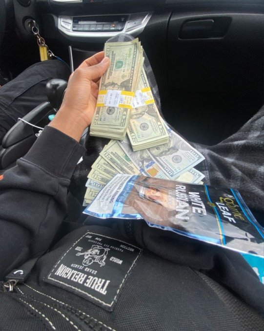 A person displays thick stacks of hundred-dollar bills banded together in a car, accompanied by a "Hype Russiang" magazine and "True Religion" wallet, visually reinforcing the post's message about outworking others to build wealth while they rest.