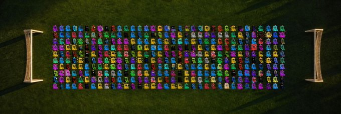 An aerial view of a large collection of colorful classic cars neatly arranged in rows on a grass field, possibly at a car show or auction lot.