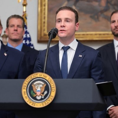 CFTC Chair Michael Selig stands at a podium bearing the presidential seal of the United States, speaking to attendees while another official in a suit stands behind him. The image illustrates the post's commentary on Selig's remarks about the growing shift toward tokenization, onchain finance, and 24/7 trading in financial markets.