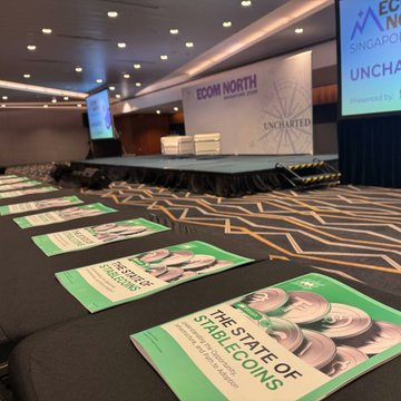 Empty chairs await attendees at the "Ecom North Singapore" conference stage, with programs for "The State of Stablecoins" lined along the seats, reflecting a recently concluded event where Morph Payments showcased their stablecoin solutions to merchants and builders.